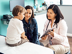 A mom and her son with a female doctor looking at an iPad screen.